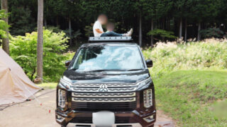 自然の中でミツビシ デリカD:5と家族が過ごすキャンプ風景。車の上に座って景色を楽しむ様子。