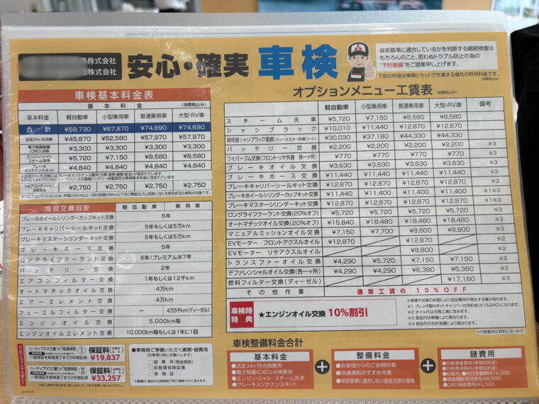 「店頭掲示の車検・メンテナンス料金ボード。左側に軽・小型・普通・大型RVの車検基本料金表（普通乗用車 合計74,690円）。中央～右側にATFやデフ、トランスファ、燃料フィルター等の作業工賃一覧。下段には交換時期の目安と費用の計算例が記載されている。撮影：2025年10月。」